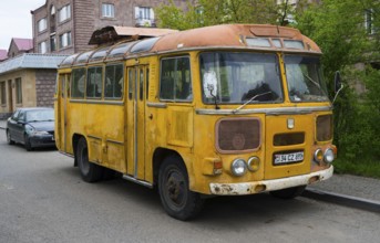 An old yellow bus stands abandoned on the street in an urban environment, clear signs of use,