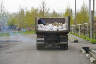 A lorry full of sacks is driven along a city street by a man in the back, exhaust fumes, Armenia