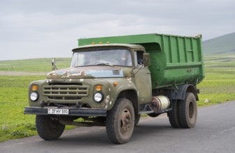 A green lorry with visible signs of wear driving on a country road in rural surroundings, ZIL-130