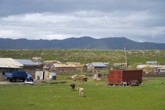 Rural settlement with huts and animals on a green pasture surrounded by mountains under a cloudy