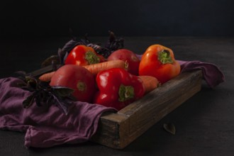 Peppers, tomatoes, carrots lie in a wooden box dark photo