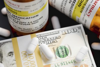 Prescription medicine bottles and pills next to stacks of 100 dollar bills