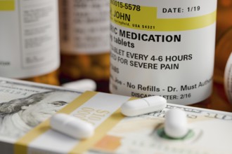 Prescription medicine bottles and pills next to stacks of 100 dollar bills