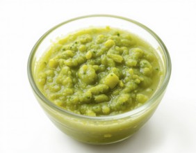 A clear glass bowl holds a thick, textured pea soup, showcasing a fresh, healthy meal. The bright