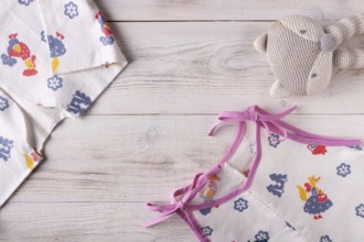 Clothes for a newborn and a rattle on a white wooden background