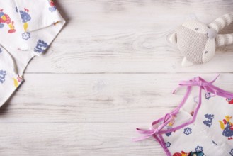 Clothes for a newborn and a rattle on a white wooden background