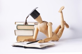 A wooden man in a student hat lies on the floor and reads textbooks