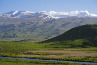 Snow-capped mountains rise above a green valley while the sky is clear and blue, landscape near Rya