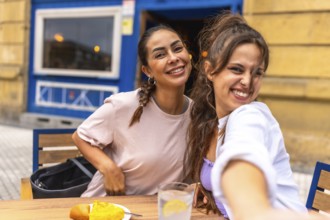 Two friends are taking a selfie while enjoying breakfast at an outdoor cafe, capturing a moment of