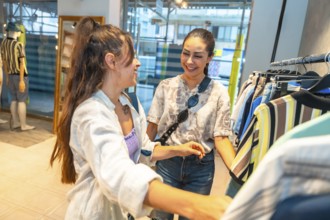 Two female customers smiling and chatting while selecting fashionable clothes in a vibrant retail