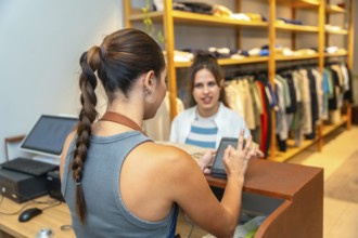 Customer making a contactless payment with her smartphone in a clothing store, assisted by the