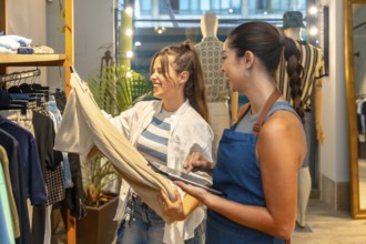 Smiling shop assistant holding tablet and showing trousers information to a happy customer in a