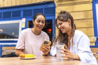 Two female friends are enjoying a moment together at a bar, looking at something funny on a