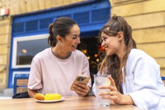 Two women are enjoying a meal and drinks at an outdoor cafe, sharing a moment of connection as they