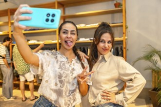 Two friends are having fun taking a selfie with a smartphone, sticking out their tongues, in a