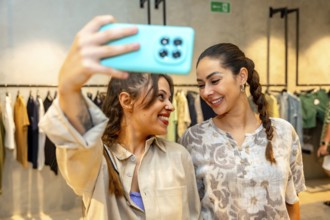 Two happy women taking a selfie with a smartphone in a clothing store, enjoying shopping and trying