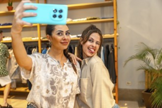 Two cheerful female customers taking a selfie with a smartphone, having fun and making funny faces