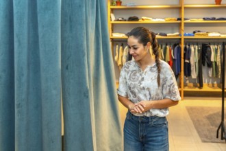 Woman trying on clothes in a store's dressing room, considering her purchase with a thoughtful