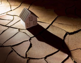 A cardboard miniature house placed on cracked, dry soil, illustrating drought, environmental