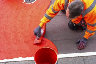 Application of red road surfacing on a cycle lane, inner-city road, so-called cold plastic