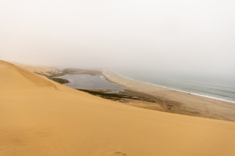 Golden dunes and the Atlantic Ocean near Namib-Naukluft Park, Namibia. A lagoon and shoreline fade