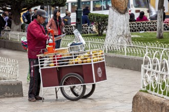 A street vendor operates a fruit stand on a pavement in a busy city, selling fresh juice in the