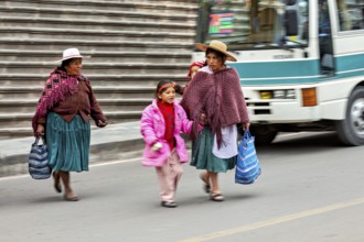 Two woman and a child in traditional dress crossing a street with stairs in the background, woman