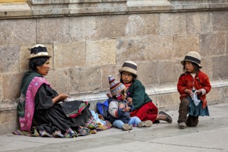 Woman and children in traditional dress sit against a stone wall, lively and colourful, woman and