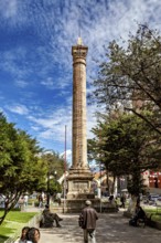 Historical pillar in the park in sunny weather surrounded by trees and people, monument and pillar