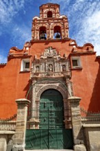 Door of a colonial building with red façade and bell tower under a clear blue sky, The churches of