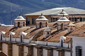 Close-up of building roofs with characteristic small domes and mountain scenery in the background,