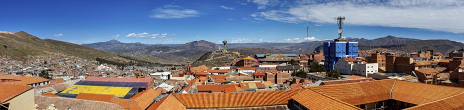 Panoramic view of a city with orange-coloured roofs, surrounded by mountains and bright sunshine,