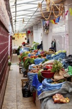 A narrow and covered market aisle full of vegetables and spices, atmospherically colourful, market