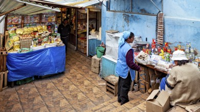 A small shop with two woman behind a table full of food in a traditional setting, market stall