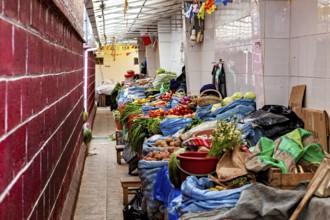 A covered market aisle full of colourful vegetables and spices in a tight arrangement, market stall