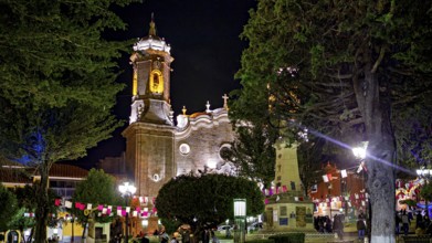 An illuminated church at night decorated with festive activities and flags, surrounded by trees,
