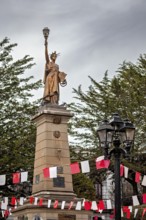 Historical statue with lantern on a high pedestal, surrounded by red and white flags and trees