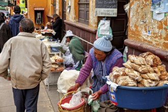 A woman sells bread at a busy street market as passers-by walk past, market stall selling goods in