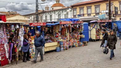 Colourful market stalls with Coca-Cola signs on a busy pavement full of people, Small market stalls