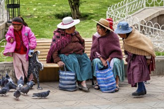 Two woman, two children on a park bench talking while pigeons are nearby, woman and people in the