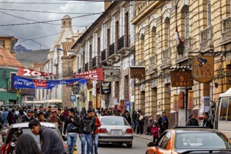 Busy street scene with colonial architecture. People and cars animate the street under a slightly