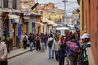Lots of hustle and bustle in a narrow city street with people walking past. Various shops and