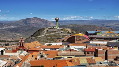 View of orange roofs with a modern building and an antenna in a mountainous environment, view over