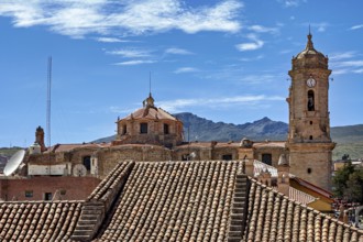 Cityscape with an old clock tower, surrounded by many roofs and mountains in the background, The