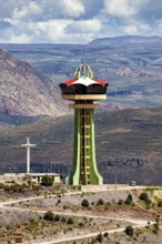 Observation tower on a hill with a cross in front of a mountain range and clouds, The water tower
