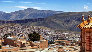 A city with tiled roofs and a mountain landscape in the background under a clear blue sky, view