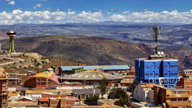 View over a city with colourful roofs and a telecommunications tower, surrounded by mountains under