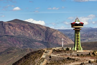 Observation tower next to cross and rocky mountain under blue sky with clouds, The water tower of