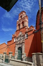 Colonial building with red façade and bell tower, surrounded by power lines and a clear sky, The