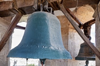 Two large bells hang in a historic bell tower with stone pillars and wooden beams, The large bell